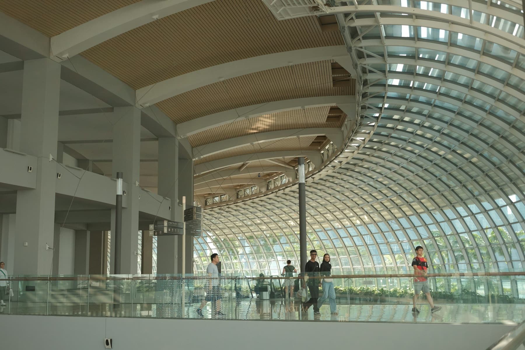 Travelers walk along a mezzanine beneath a sweeping curved glass roof